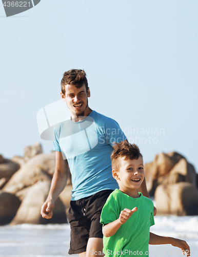 Image of happy family on beach playing, father with son walking sea coast, rocks behind smiling enjoy summer