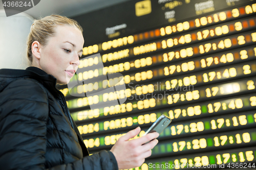 Image of Woman at airport in front of flight information board checking her phone.