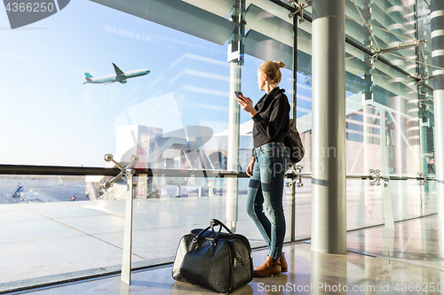 Image of Young woman waiting at airport, looking through the gate window.