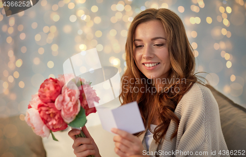 Image of happy woman with flowers and greeting card at home