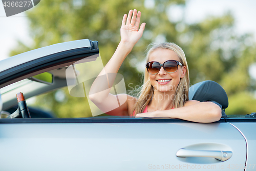 Image of happy young woman in convertible car waving hand