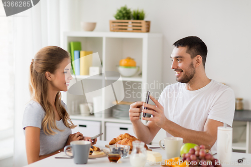 Image of couple with smartphones having breakfast at home