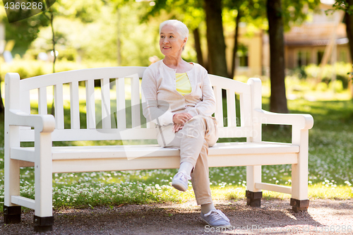 Image of happy senior woman sitting on bench at summer park