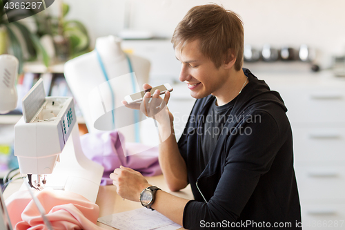 Image of fashion designer with smartphone working at studio