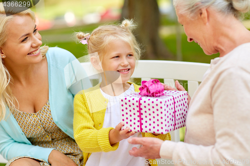 Image of happy family giving present to grandmother at park
