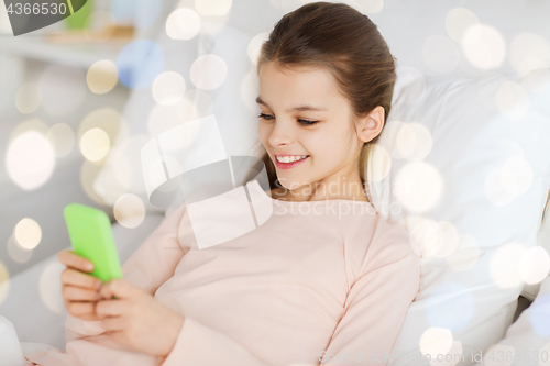 Image of happy girl in bed with smartphone over lights