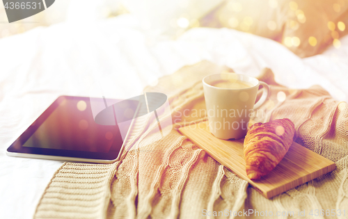 Image of tablet pc, coffee and croissant on bed at home