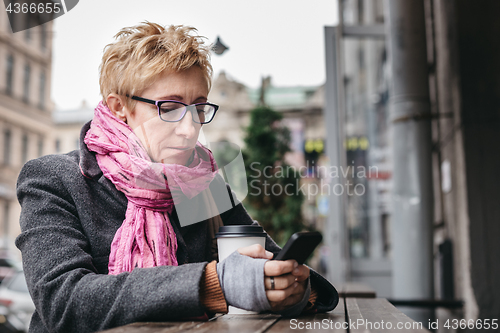 Image of Woman browsing smartphone in outside cafe