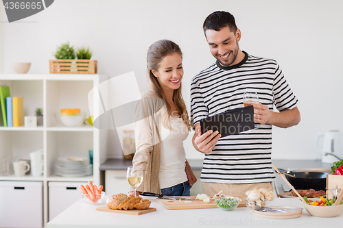 Image of happy couple with tablet pc cooking food at home