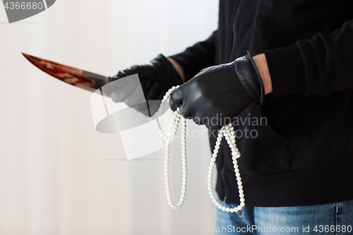 Image of criminal with knife and jewelry at crime scene