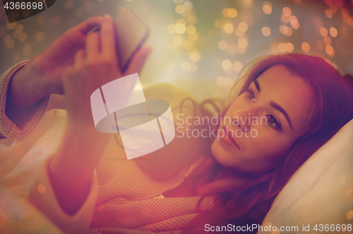 Image of young woman with smartphone in bed at home bedroom