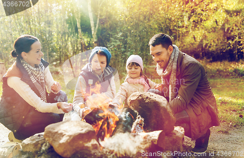 Image of happy family roasting marshmallow over campfire