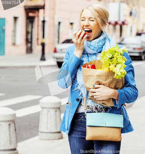 Image of young pretty blond woman with food in bag walking on street