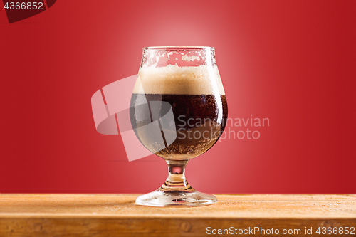 Image of glass of cold frothy dark beer on an old wooden table