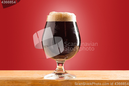 Image of glass of cold frothy dark beer on an old wooden table