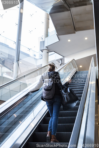 Image of Businesswoman with large black bag and mobile phone ascending on escalator.