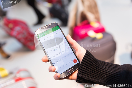 Image of Woman checking calendar information on mobile phone sitting in airport terminal.