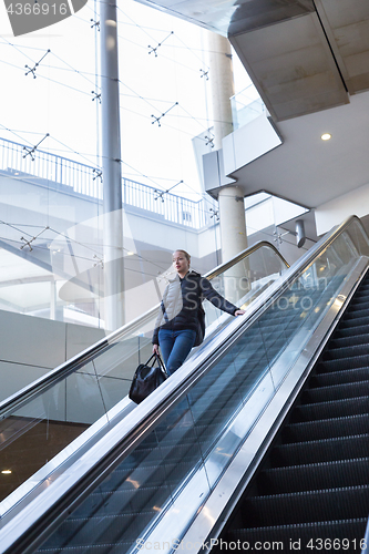 Image of Businesswoman with large black bag and mobile phone descending on escalator.