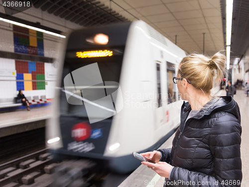 Image of Woman with a cell phone waiting for metro.