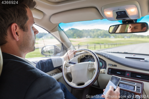 Image of Businessman using cell phone and texting while driving not paying attention to the road.