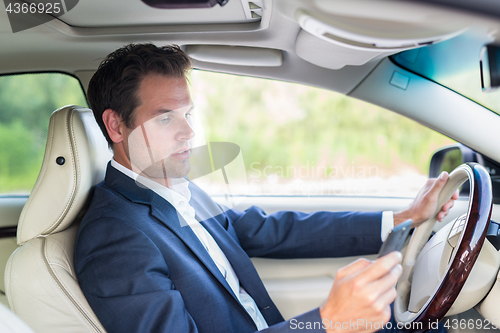 Image of Businessman using cell phone and texting while driving not paying attention to the road.