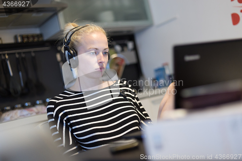 Image of Adult woman in her casual home clothing working and studying remotely from her small flat late at night.