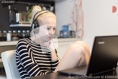 Image of Adult woman in her casual home clothing working and studying remotely from her small flat late at night.