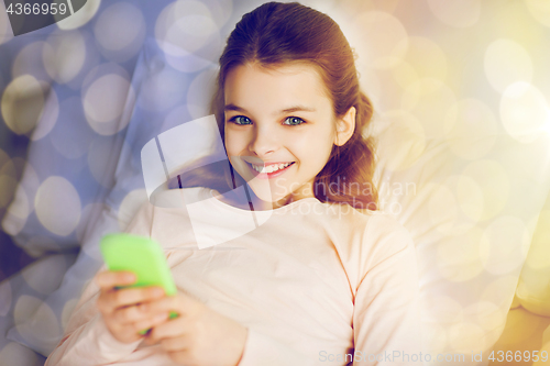 Image of happy girl in bed with smartphone over lights