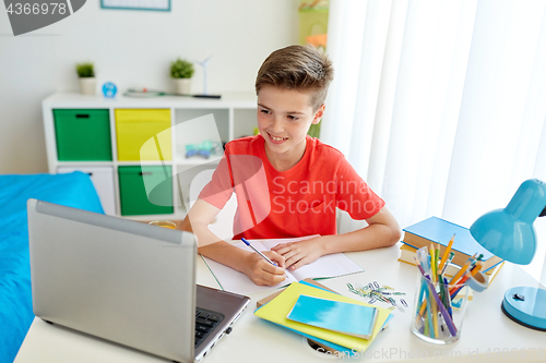 Image of student boy with laptop writing to notebook