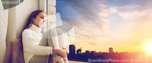 Image of sad girl sitting on sill at home window