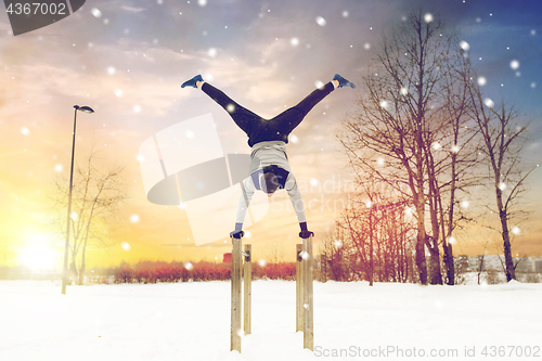 Image of young man exercising on parallel bars in winter