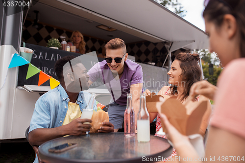 Image of happy friends with drinks eating at food truck