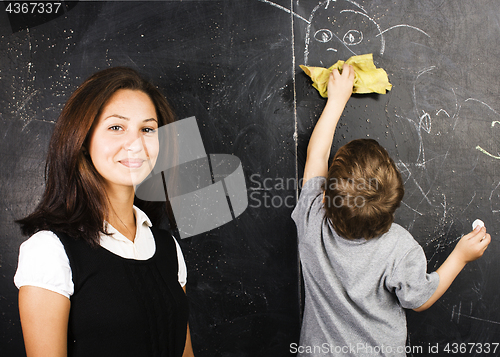 Image of little cute boy in glasses with young real teacher, classroom studying at blackboard school kido