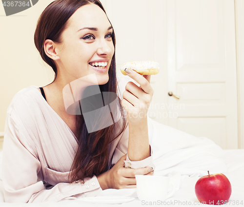 Image of young pretty brunette woman laying in bed, luxury white interior