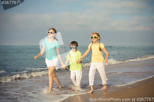 Image of Three happy children running on the beach at the day time.