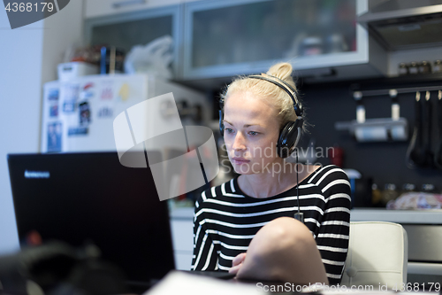 Image of Adult woman in her casual home clothing working and studying remotely from her small flat late at night.