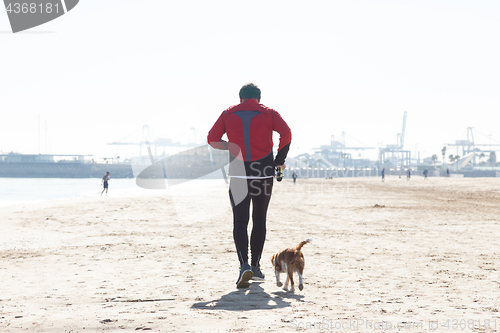 Image of Senior Man Exercising On Beach With His Dog Running Next To Him.