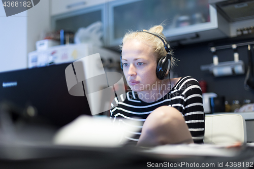 Image of Adult woman in her casual home clothing working and studying remotely from her small flat late at night.