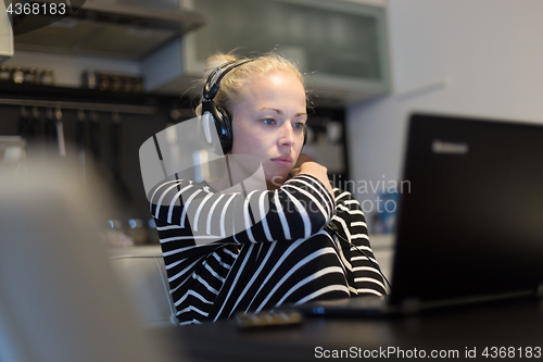 Image of Adult woman in her casual home clothing working and studying remotely from her small flat late at night.