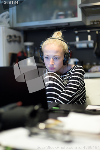 Image of Adult woman in her casual home clothing working and studying remotely from her small flat late at night.