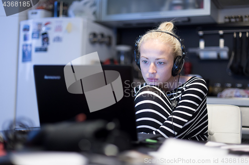 Image of Adult woman in her casual home clothing working and studying remotely from her small flat late at night.