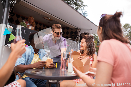 Image of happy friends with drinks eating at food truck