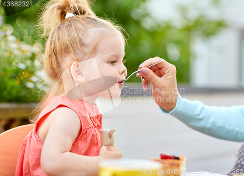 Image of mother hand with spoon feeding daughter at cafe