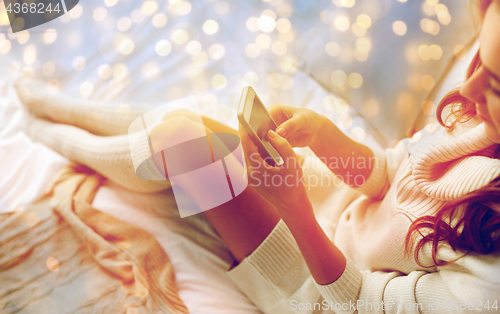 Image of happy young woman with smartphone in bed at home