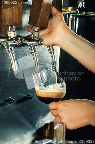 Image of Hand of bartender pouring a large lager beer in tap.