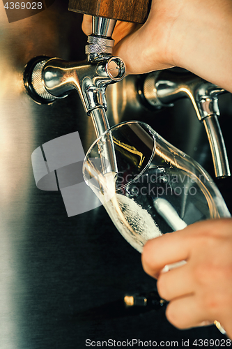 Image of Hand of bartender pouring a large lager beer in tap.