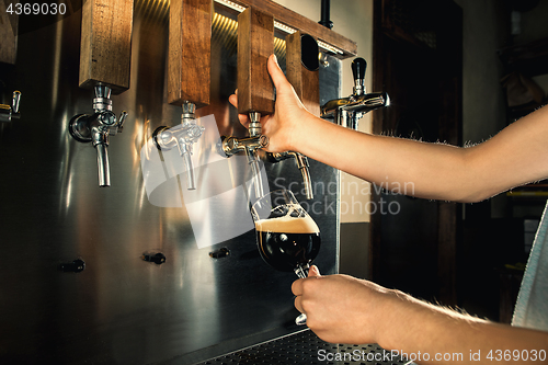 Image of Hand of bartender pouring a large lager beer in tap.