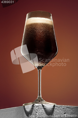 Image of glass of cold frothy dark beer on an old wooden table