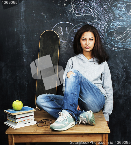 Image of young cute teenage girl in classroom at blackboard seating on ta