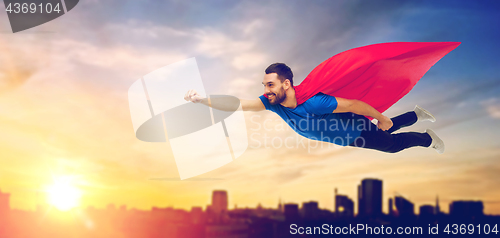 Image of happy man in red superhero cape flying over city